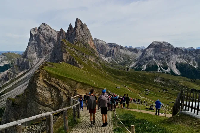 Walkers on the path along Seceda's tilted grass ridge, which drops away into the Odle spires