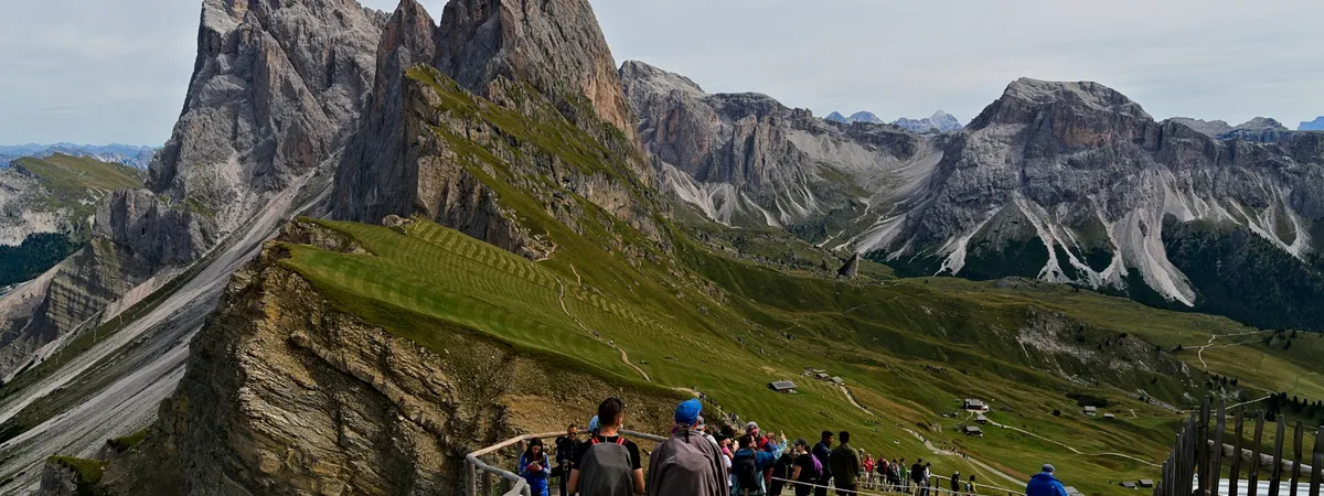 Walkers on the path along Seceda's tilted grass ridge, which drops away into the Odle spires