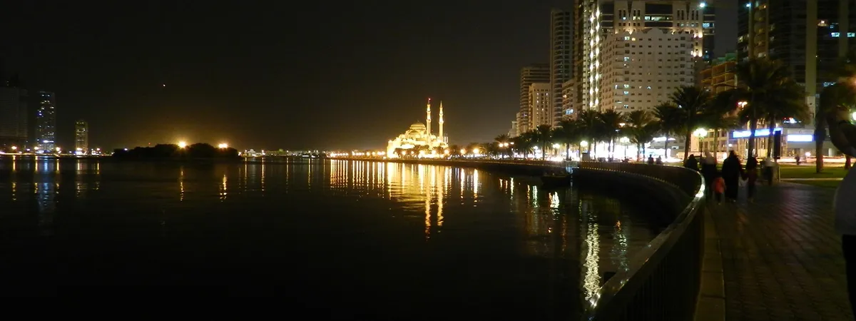 Al Noor Mosque lit up at night, reflected in the water of Khalid Lagoon along Sharjah's Corniche