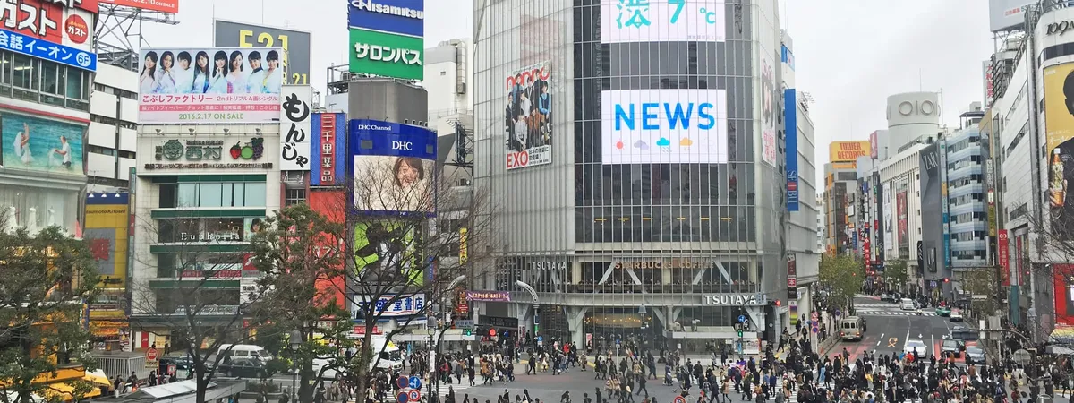 Crowds crossing the Shibuya Scramble Crossing surrounded by illuminated billboards