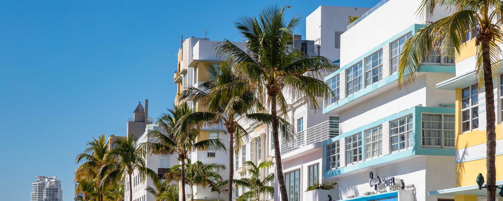 Pastel-colored Art Deco hotels, including the Penguin Hotel, lining Ocean Drive in South Beach behind a row of palm trees