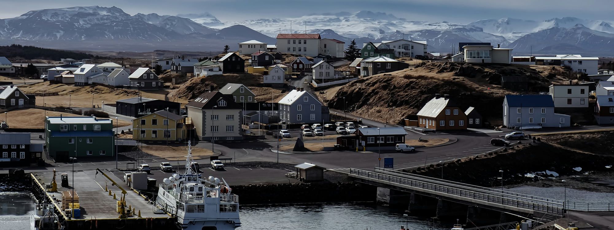 Stykkishólmur harbor with the Breiðafjörður ferry at the pier, colorful timber houses on the ridge above and snow-capped Snæfellsnes mountains beyond