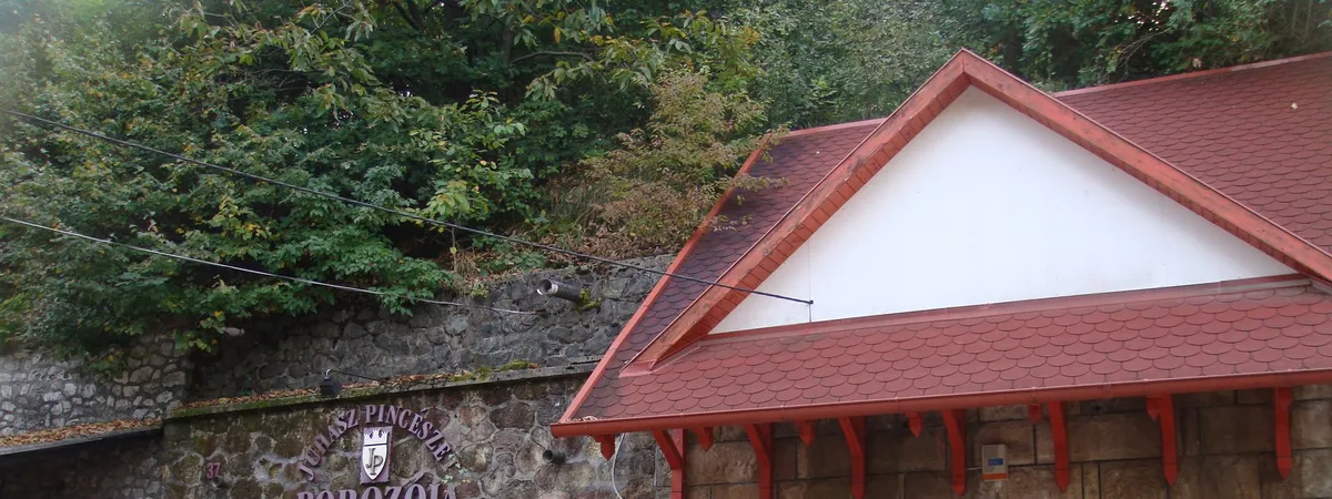 A gabled wine-cellar building with a red tiled roof set into the wooded hillside of Szépasszony-völgy outside Eger