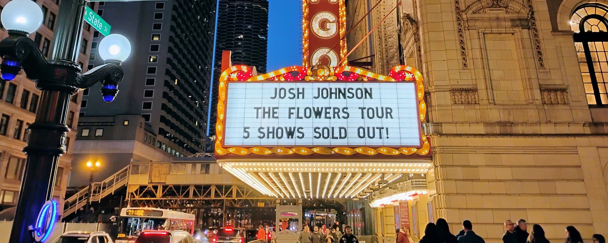 The Chicago Theatre's illuminated marquee on State Street at dusk, with an elevated 'L' train station visible behind it