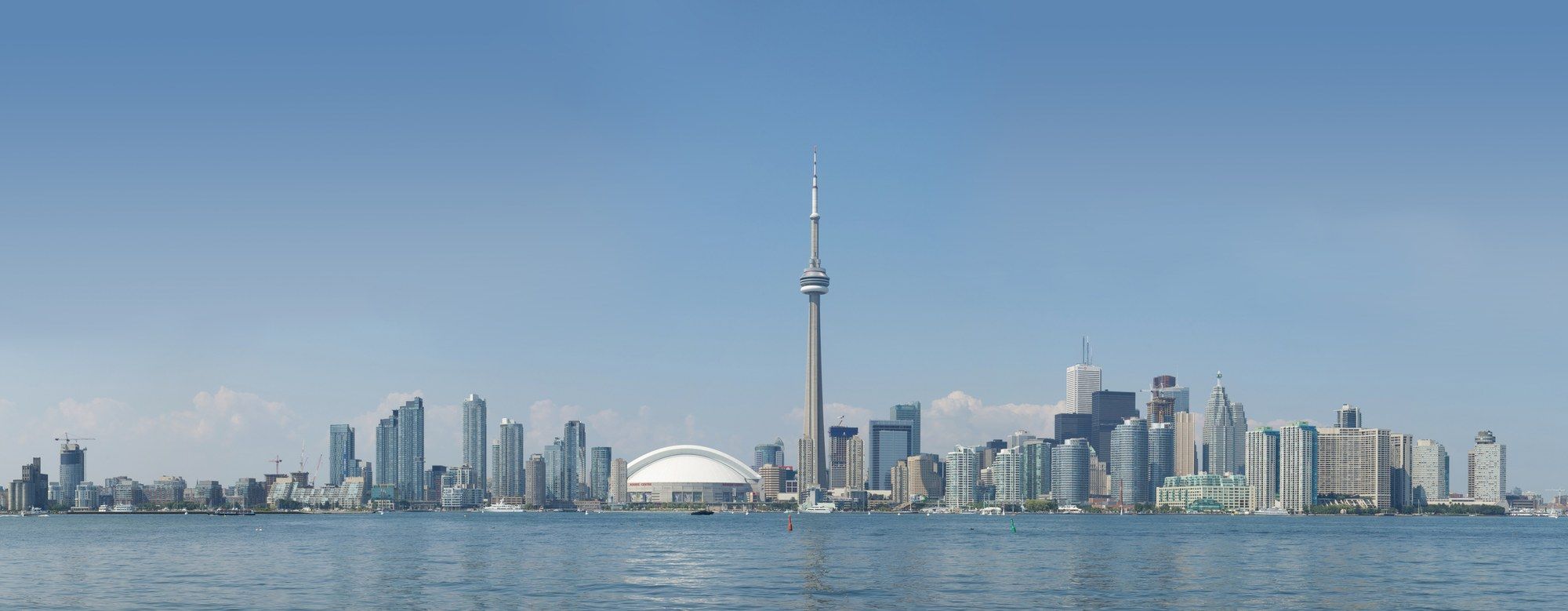 Toronto skyline seen across the water from Centre Island, with the CN Tower rising above the downtown towers and Rogers Centre's dome
