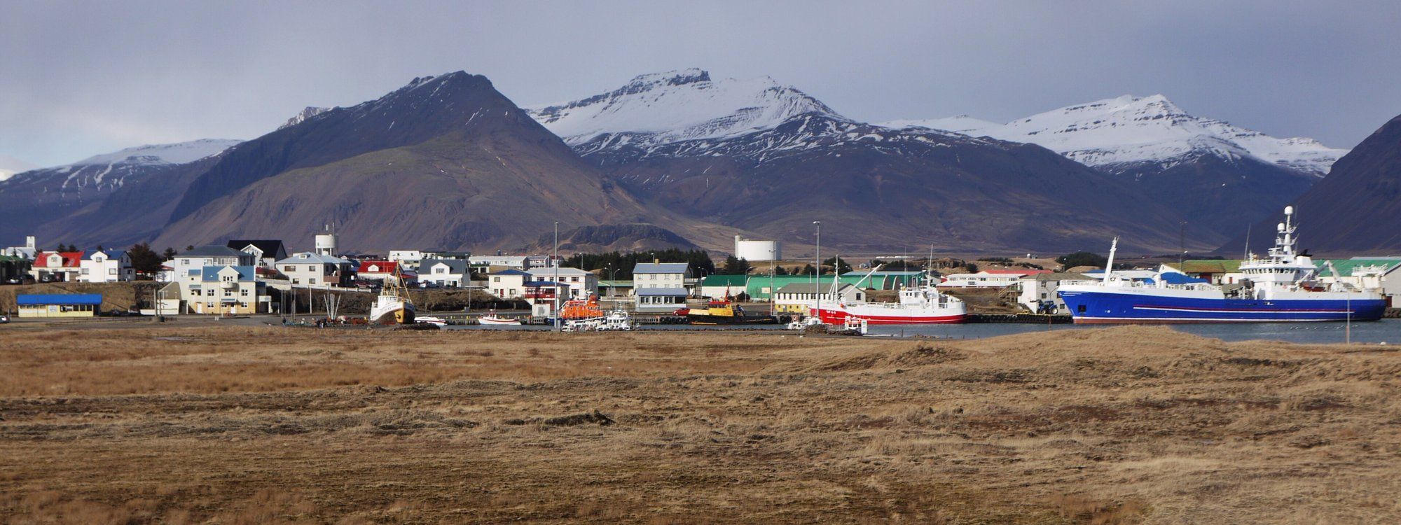 Fishing boats moored in Höfn's harbor with mountains rising in the background under a clear sky