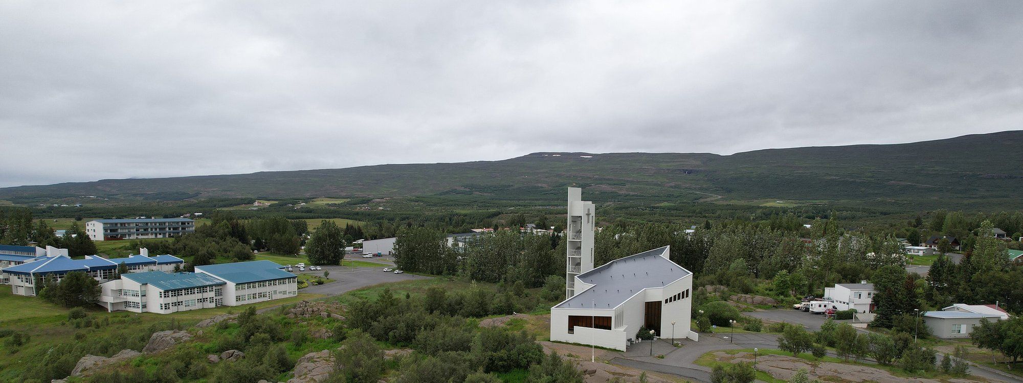 Egilsstaðakirkja, the town's modern white church, on a rocky, tree-covered rise above the surrounding buildings and valley
