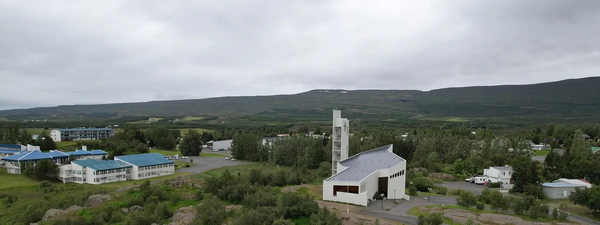 Egilsstaðakirkja, the town's modern white church, on a rocky, tree-covered rise above the surrounding buildings and valley