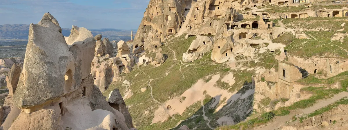 Uçhisar Castle, a tall natural rock citadel honeycombed with carved windows and doorways, rising above the surrounding village