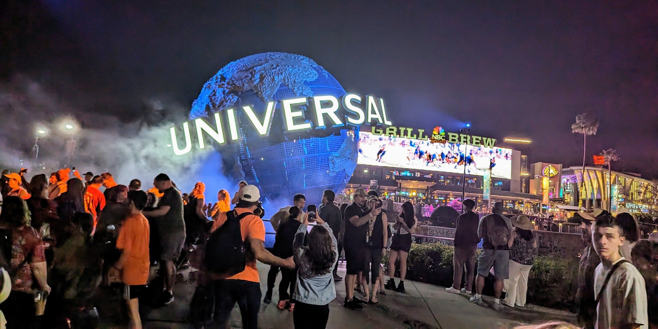 The illuminated, rotating Universal Studios globe at the entrance to Universal Orlando, with CityWalk's restaurants lit up behind it at night