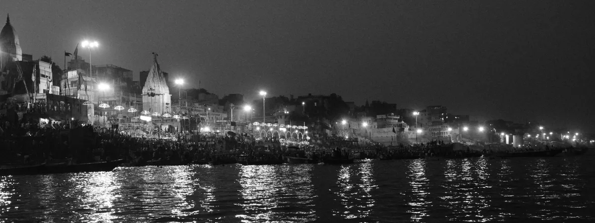 The ghats of Varanasi lit up at dusk along the Ganges, with the spire of a riverside temple rising above the crowds