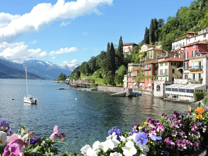 Varenna's pastel waterfront houses stepping down to Lake Como, a sailing boat moored offshore and mountains beyond