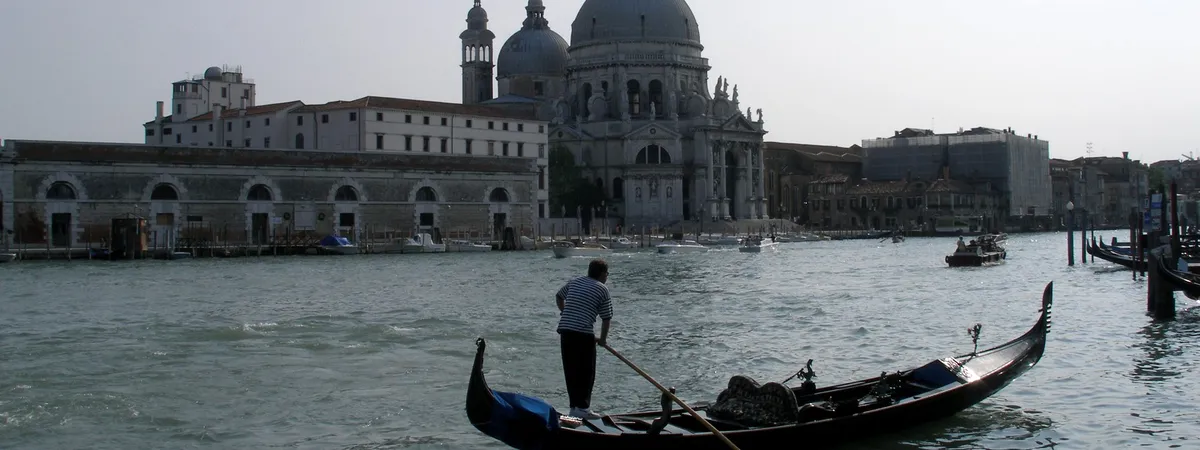 A gondolier poling along the Grand Canal in Venice, with the domed Basilica of Santa Maria della Salute in the background