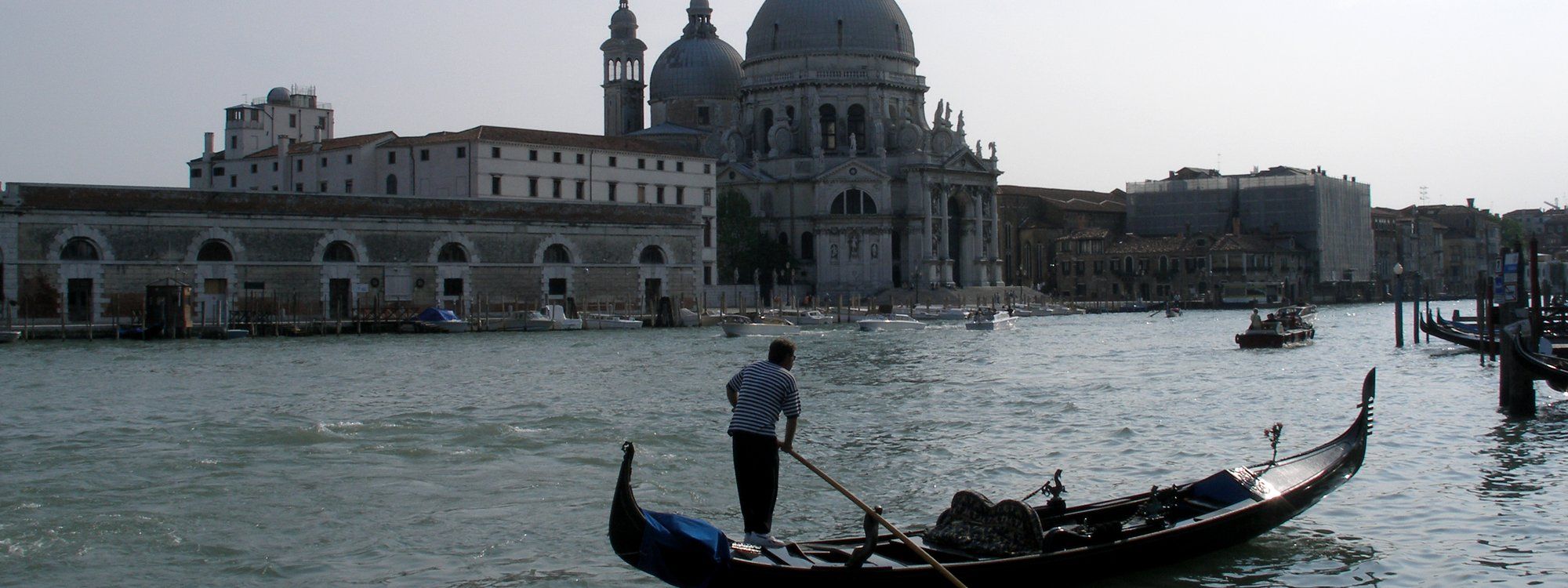A gondolier poling along the Grand Canal in Venice, with the domed Basilica of Santa Maria della Salute in the background
