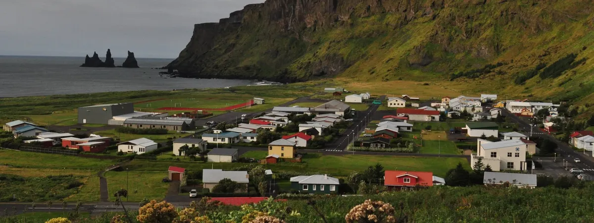 Vík's small grid of houses and streets beneath green cliffs, with the Reynisdrangar sea stacks visible offshore