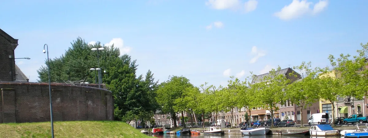 The Wittevrouwensingel canal in Utrecht, lined with trees and moored boats beside the old Wolvenplein prison wall