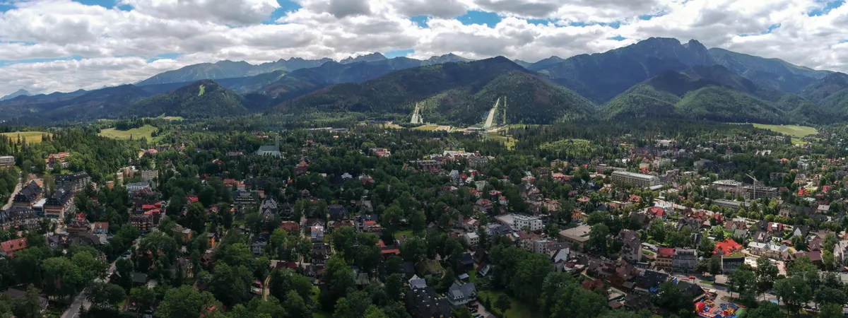 Aerial view of Zakopane spread across a forested valley, with the Wielka Krokiew ski jump towers and the Tatra Mountains rising behind the town