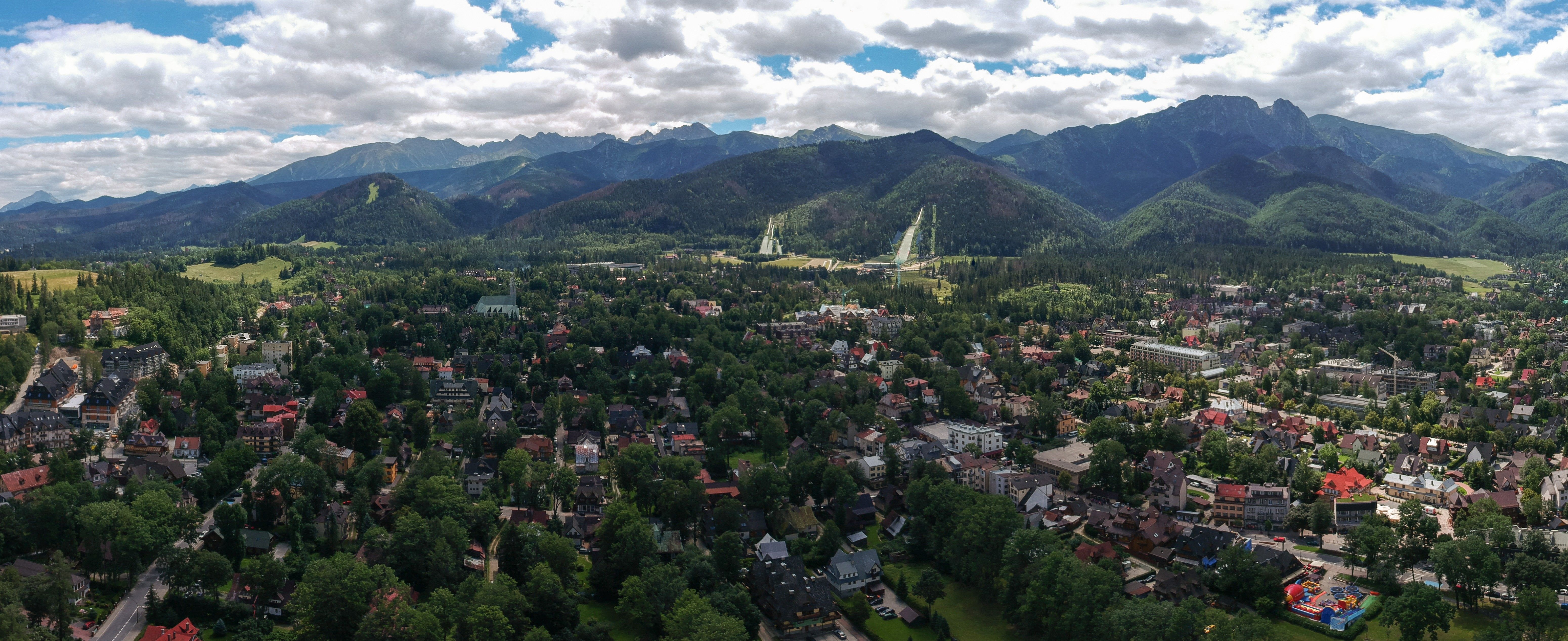 Aerial view of Zakopane spread across a forested valley, with the Wielka Krokiew ski jump towers and the Tatra Mountains rising behind the town