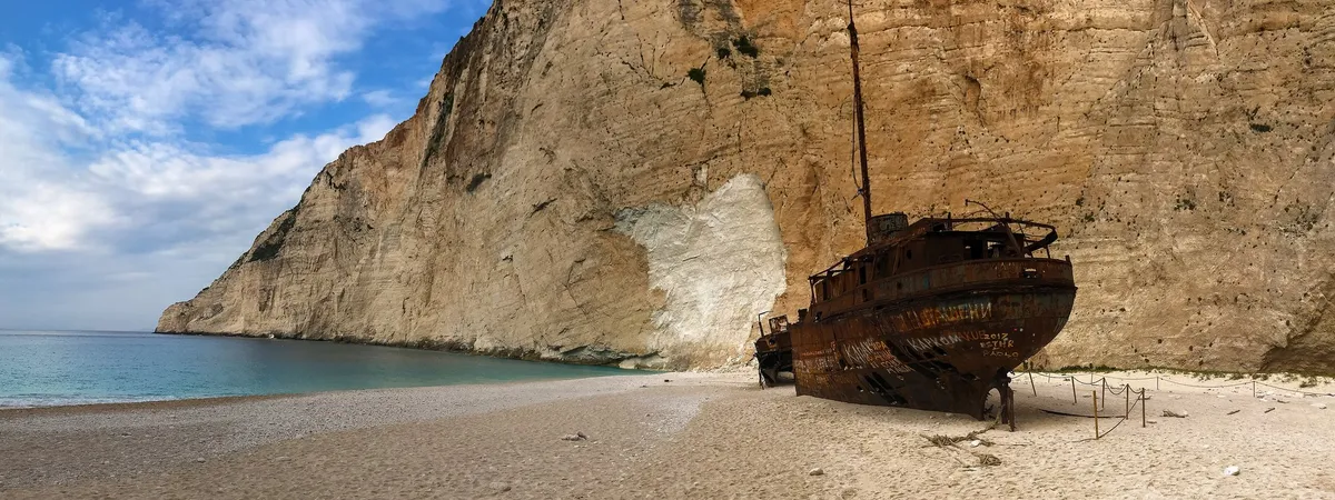 El oxidado naufragio del Panagiotis sobre la arena blanca de la playa de Navagio, enmarcado por altos acantilados de caliza
