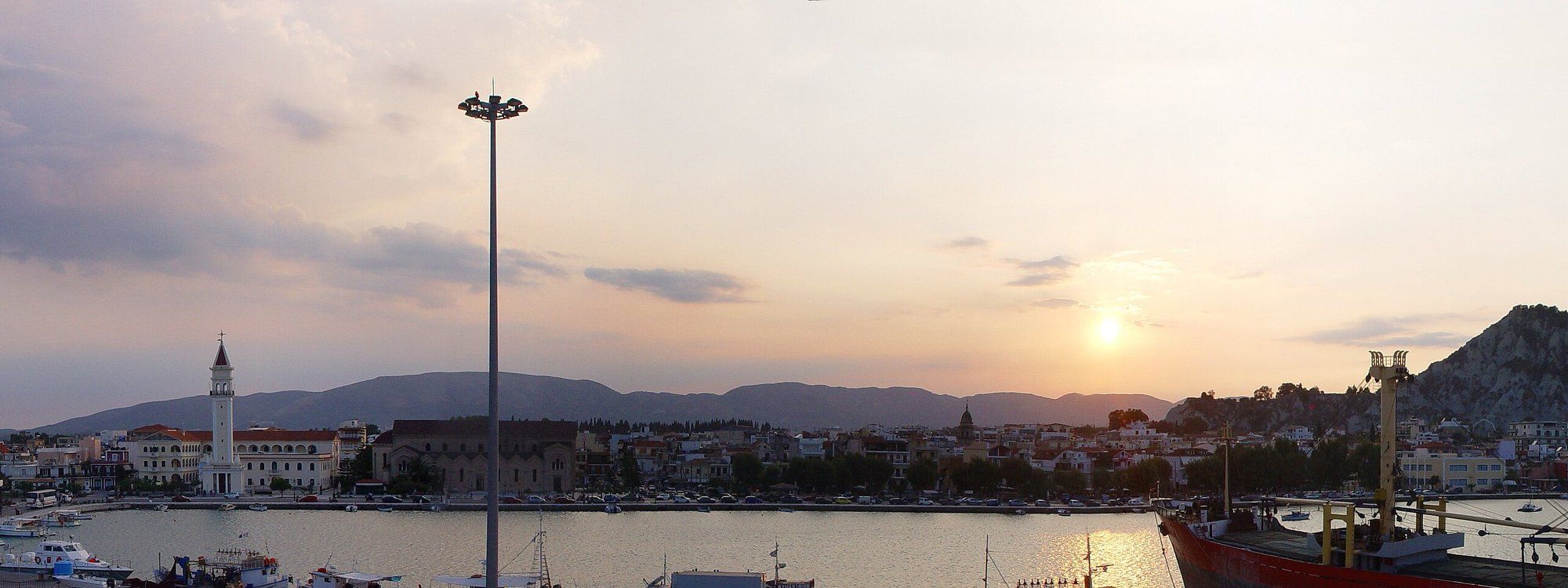 El puerto de la Ciudad de Zante al atardecer, con el campanario de la iglesia de Agios Dionysios y la ciudad respaldada por colinas